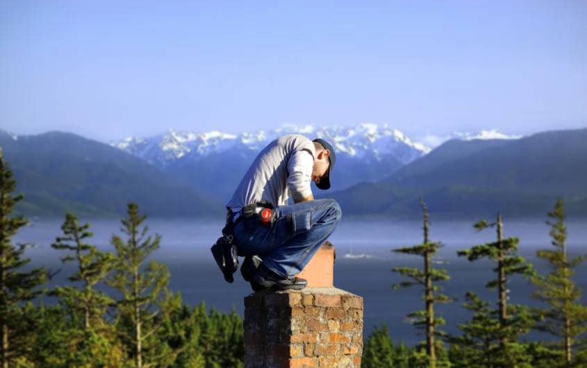 Your chimney sweep at work on top of a masonry chimney, with the Sound and mountains behind